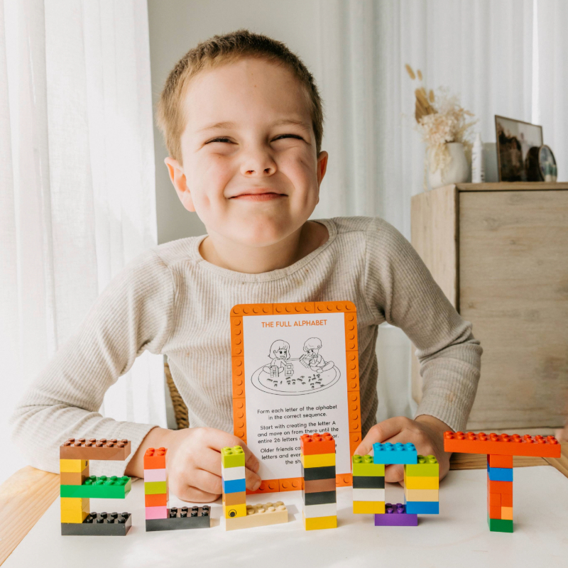 Smiling child proudly showing letters built from colourful bricks